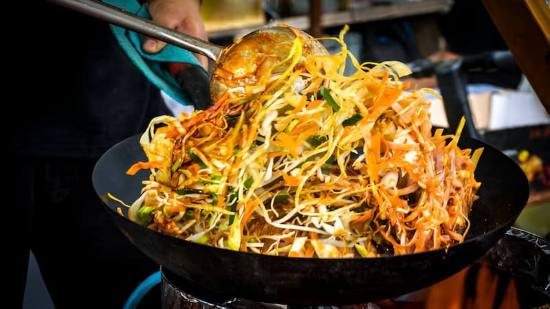 A vendor cooks pad thai with shrimp and noodles in a flaming wok at a Bangkok street stall.
