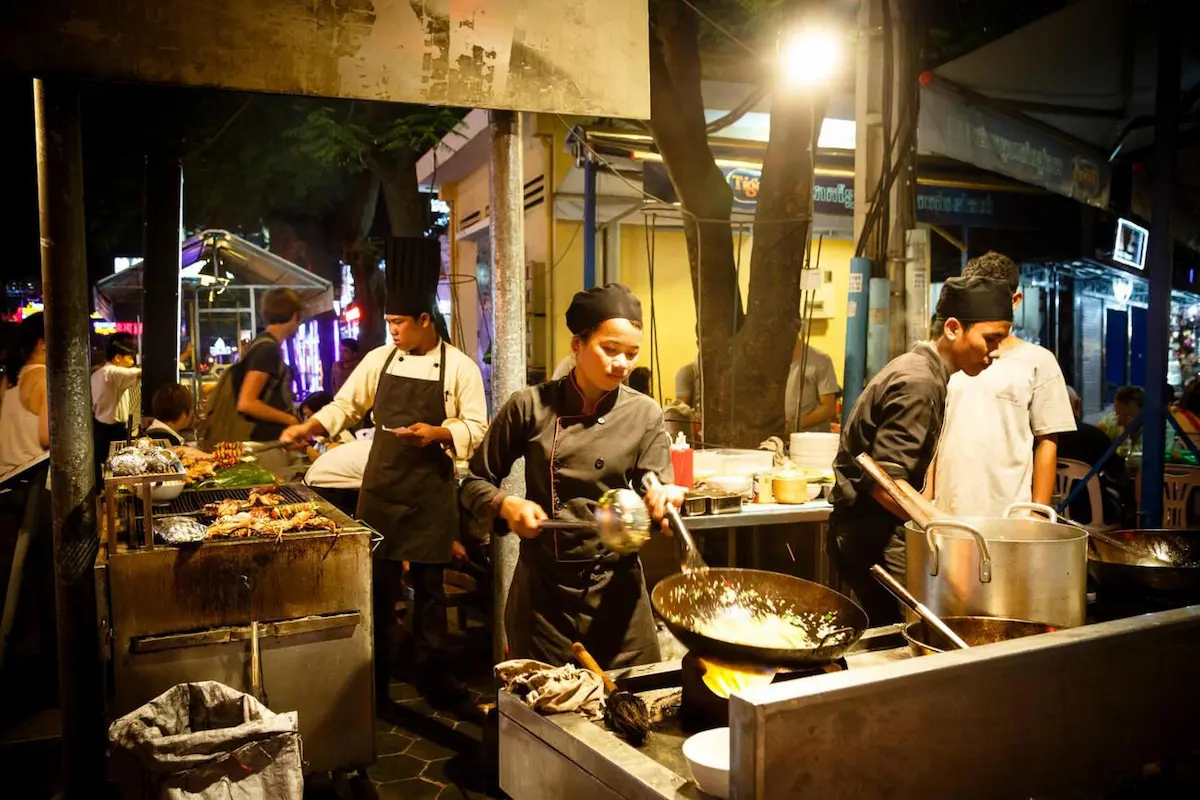 Cambodian street food chef cooking in a large wok at an outdoor market, preparing affordable local dishes that make Cambodia Southeast Asia's budget travel hotspot