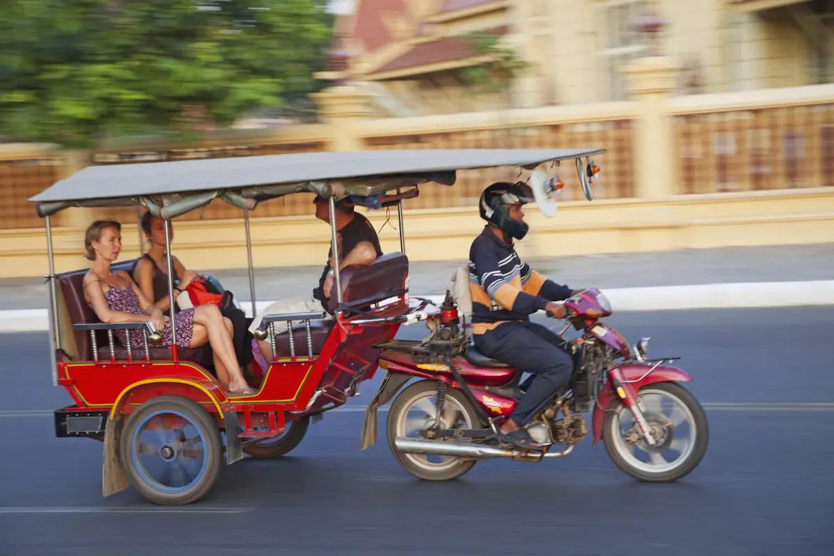 Motorbike taxi (moto-dop) carrying a passenger through a Cambodian street, offering the most affordable transportation option at just $1 for short trips around town