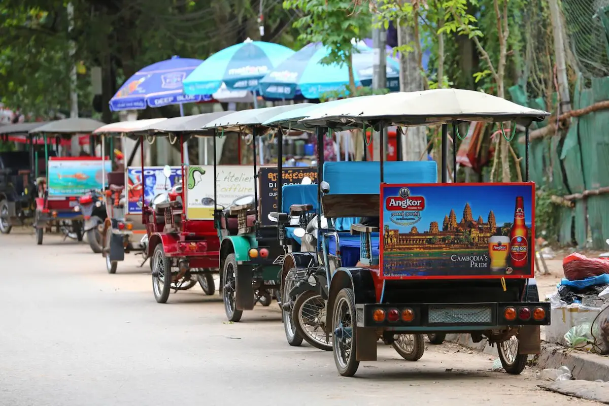 Colourful tuk-tuks lined up under shade umbrellas in Cambodia, offering budget-friendly transportation for travelers at $1-3 per ride, significantly cheaper than taxis in other Southeast Asian countries