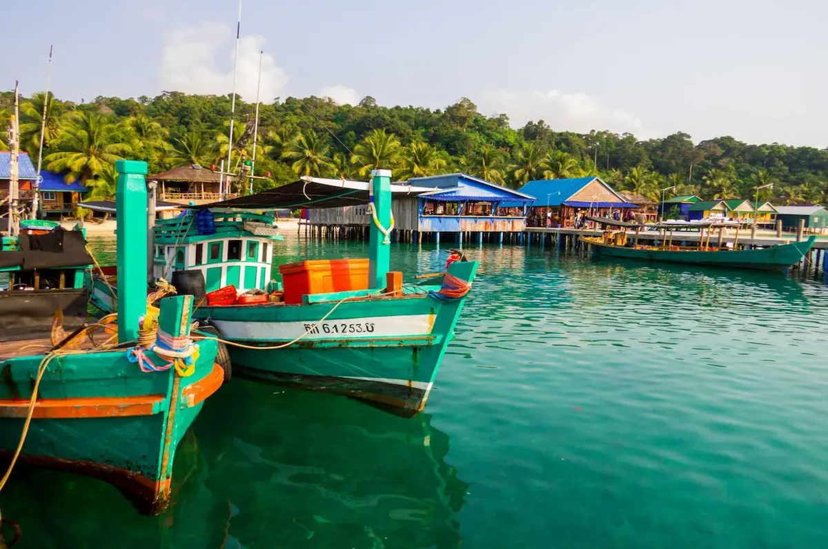 Colorful traditional Cambodian fishing boat in Koh Rong's turquoise harbor where budget travelers can arrange island-hopping tours for just $10-15, compared to $30-45 for similar experiences in Thailand