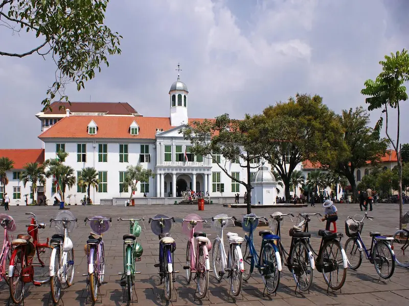 Museum Fatahillah, a Dutch colonial-style building in Jakarta’s historic Kota Tua (Old Town), with people walking and cycling in the surrounding plaza.